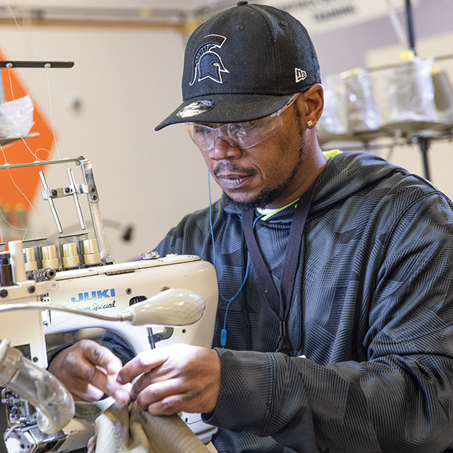 Production floor employee sews garments at Peckham Inc.