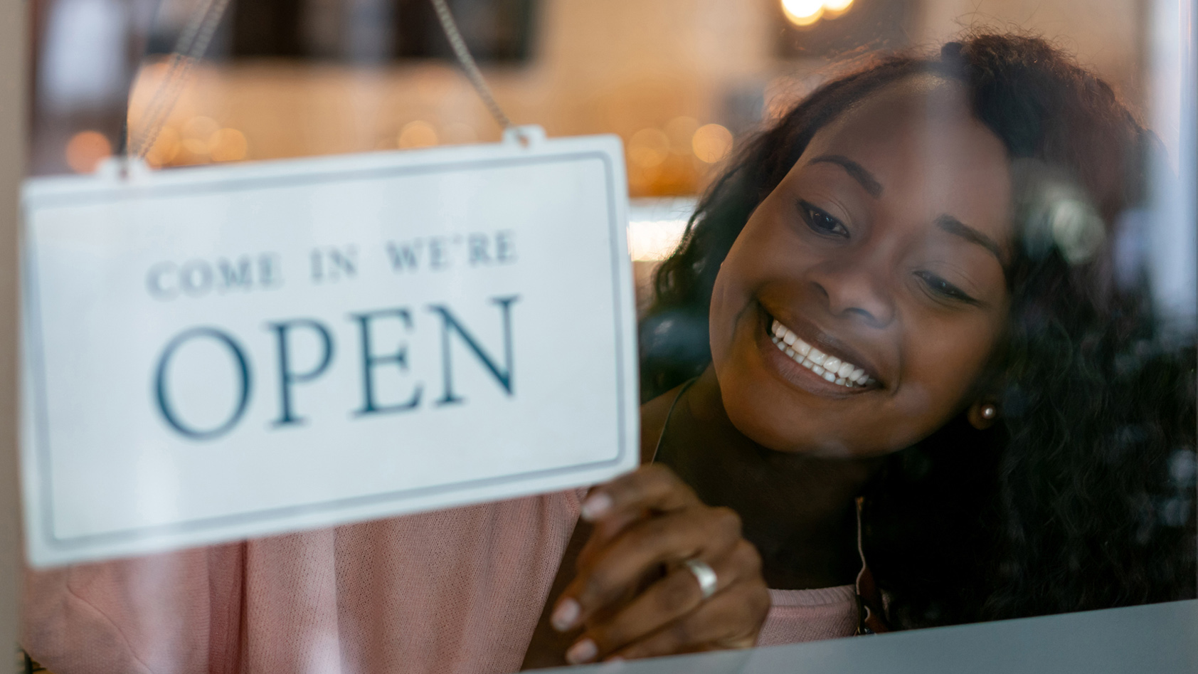 A young woman places "come in we're open" sign in her business window