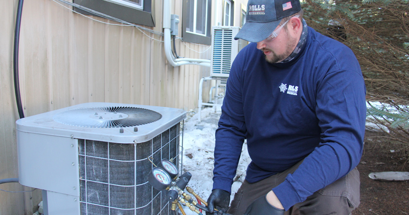 Technician from Rolls Mechanical works on an air conditioner