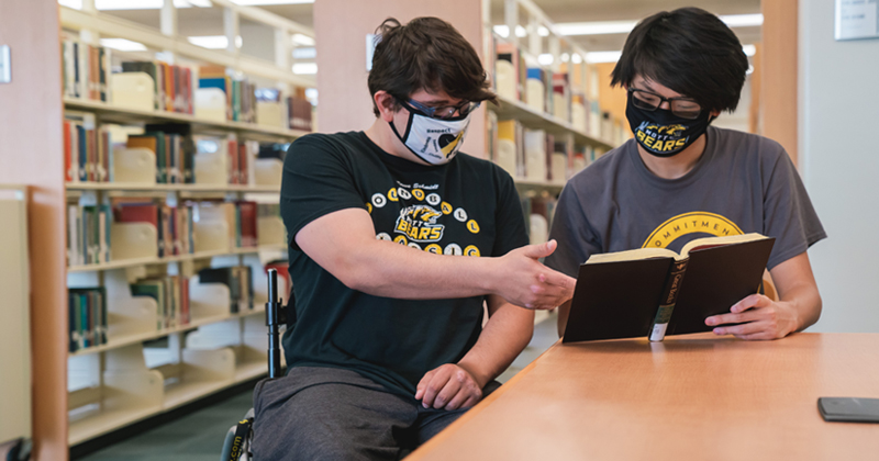 A wheelchair bound Mott Community College student meets with another student in library