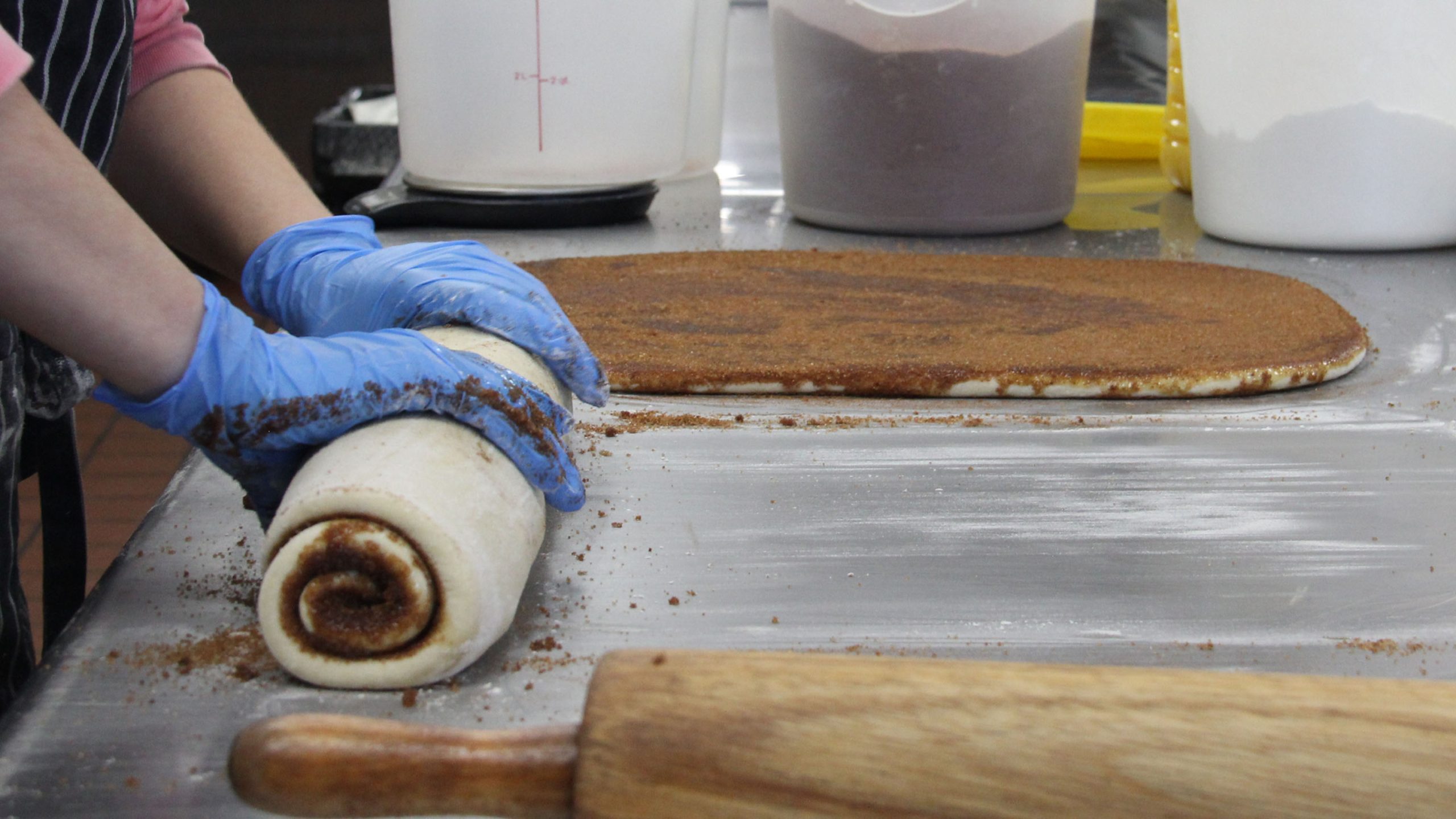 A baker rolls up sweet dough filled with cinnamon to be cut into cinnamon rolls