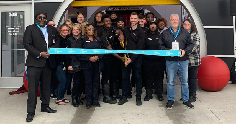 The owners of Tommy's Express Car Wash and many employees cut a ribbon outside the exit door of Tommy's Express Car Wash