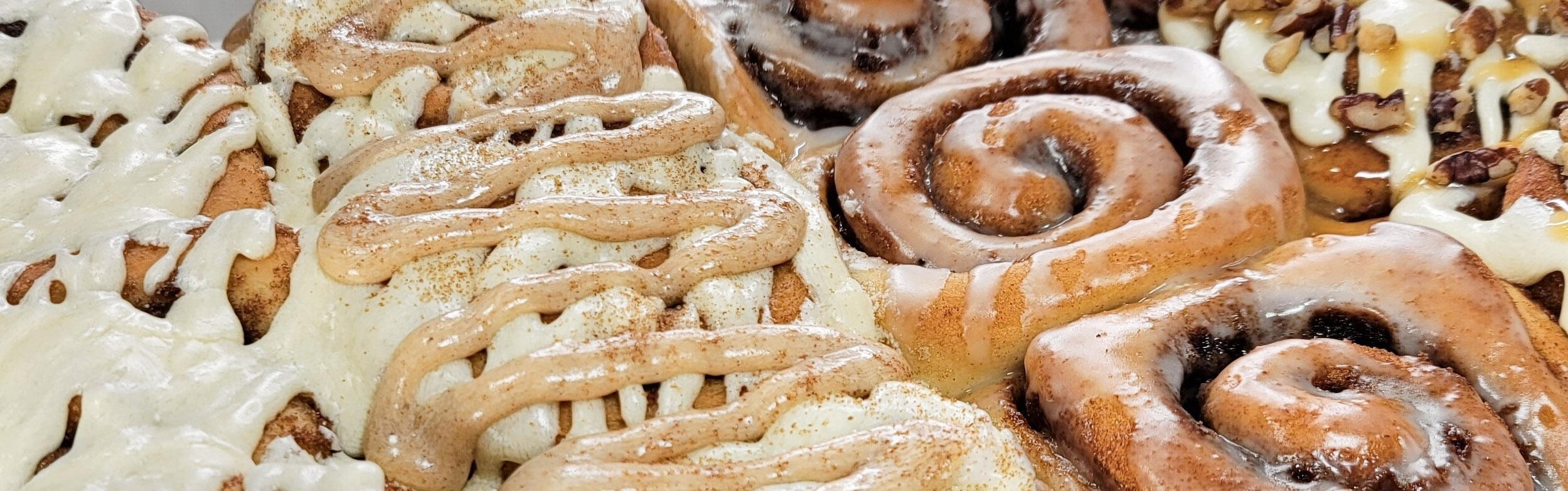 A tray of cinnamon rolls decorated with different icing including cinnamon, buttercream and pecan.