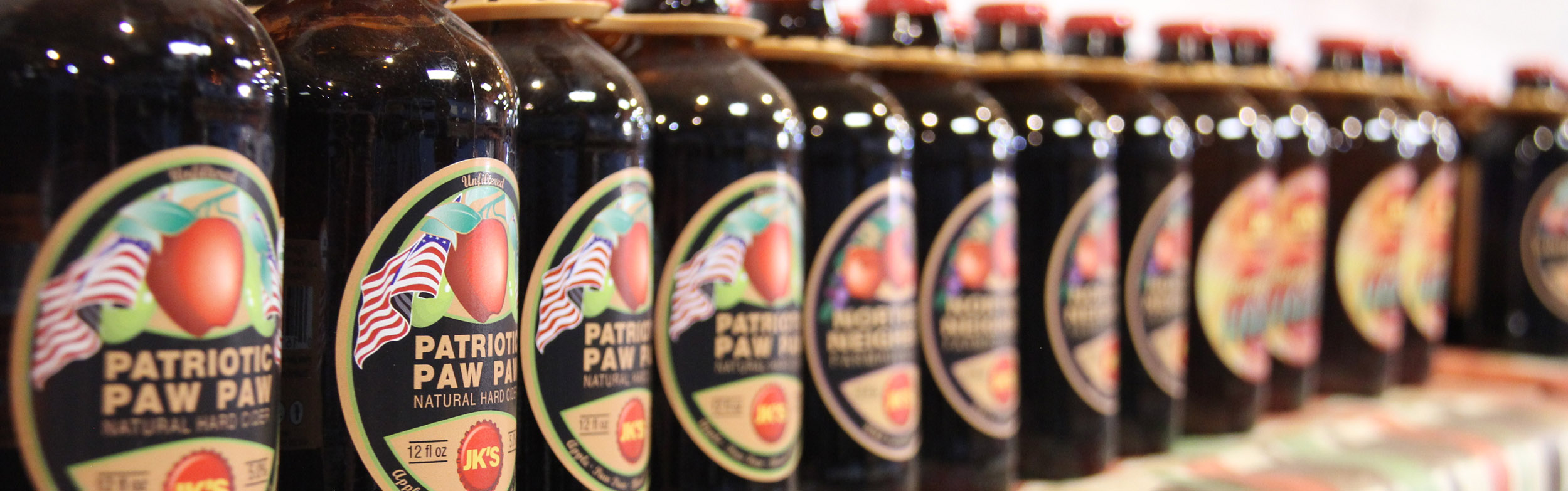 A shelf inside the Almar Orchards fruit market is lined with a row of Patriot Paw Paw hard cider growlers.