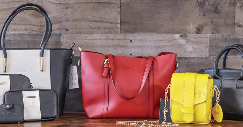 A collection of leather bags - a black and white collection of purse, clutch and wallet, a red large purse, a yellow cross body bag, and black hand bag are displayed on a table.