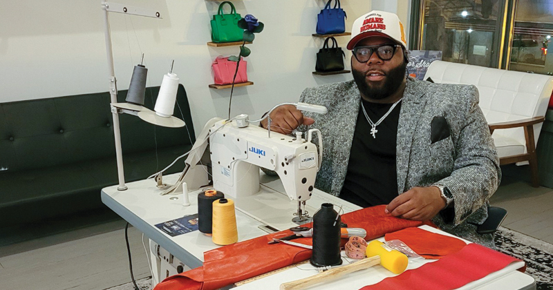 Miracle McGlown sits at his sewing machine to sew pieces of orange leather together for his next leather bag.