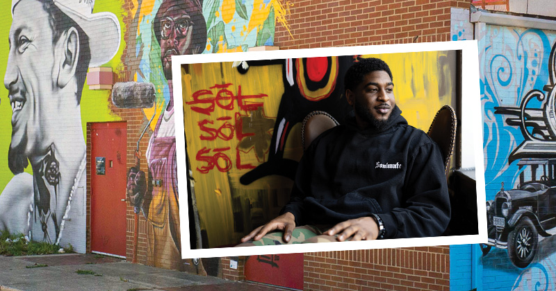 Channing Pearson, designer of Soulmate streetwear, sits on a lounge chair looking out the window inside Bau-Hause retail shop. Pearson wears his black hoodie with Soulmate logo on the left chest. Behind him is a bright yellow and red graphic.