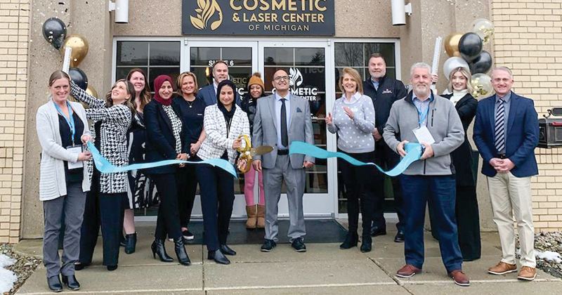 Employees and guests of Cosmetic & Laser Center of Michigan line outside the front door of their entrance and cut a ribbon with over-size scissors for the grand opening.