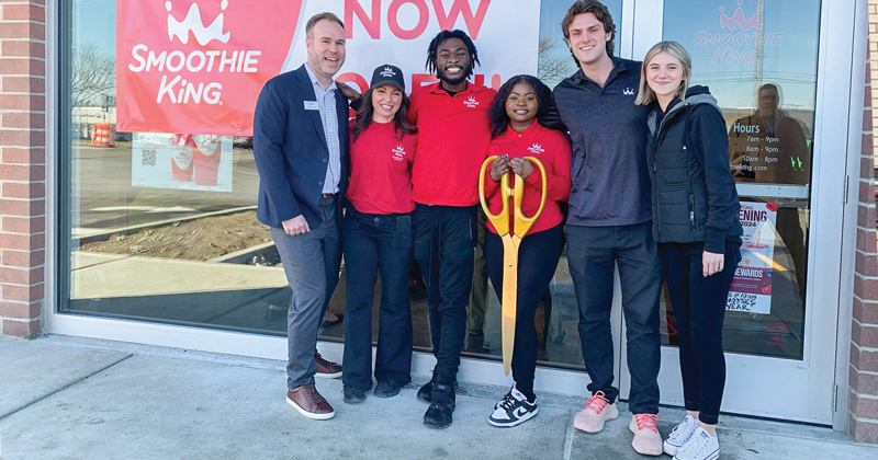 A chamber staff member joins five employees of Smoothie King outside the entrance of their new location for a ribbon cutting.