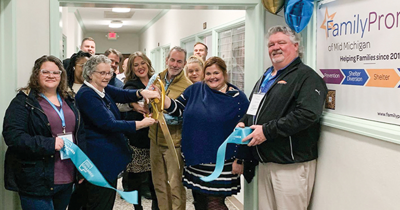 Employees of Family Promise gathered inside in the hallway to cut the ribbon with large gold scissors on the opening.