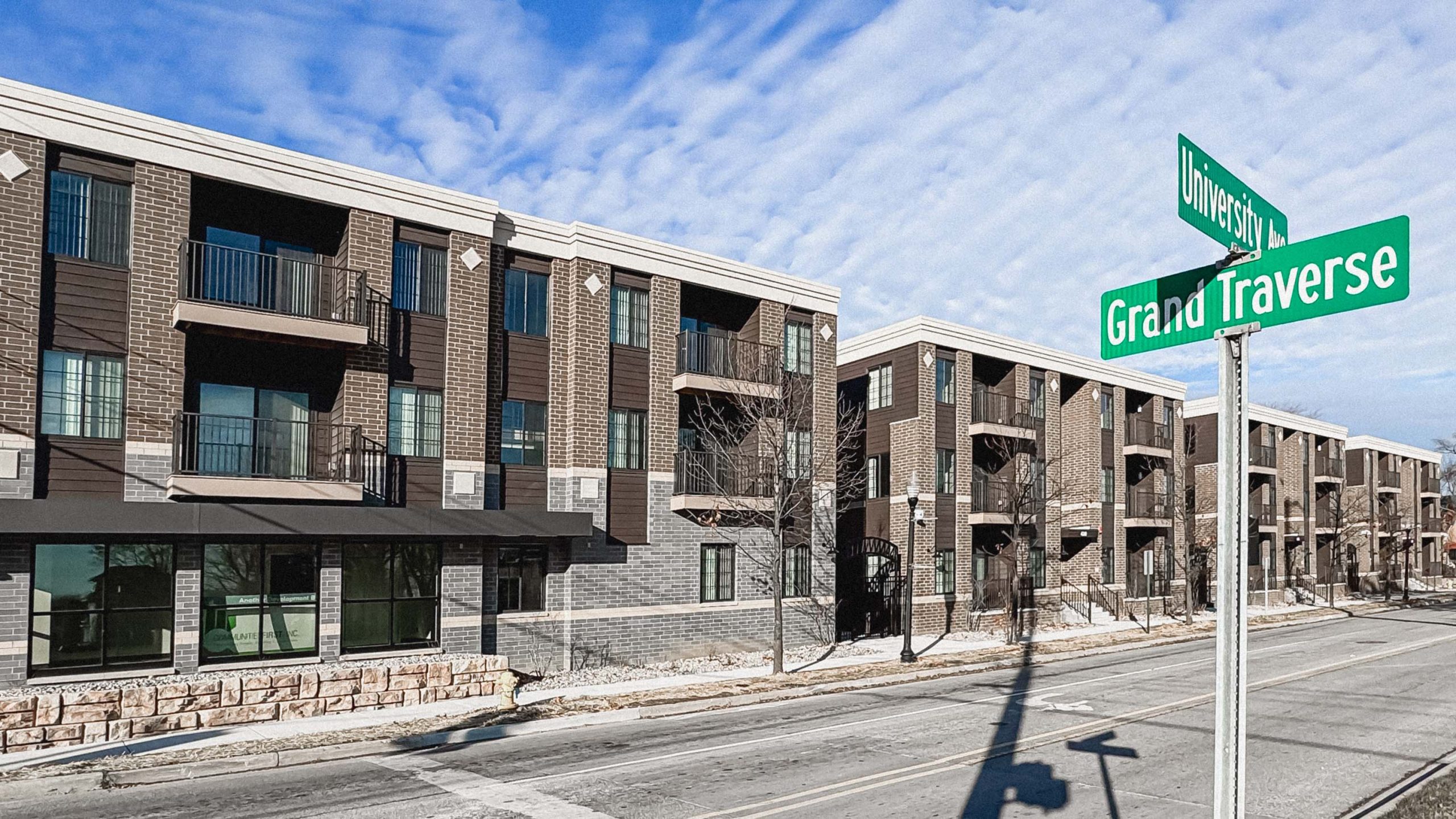 Street view of the Grand on University, a brick mixed-use, mixed-income development in Carriage town. The street sign locates this at University Ave. and Grand Traverse.