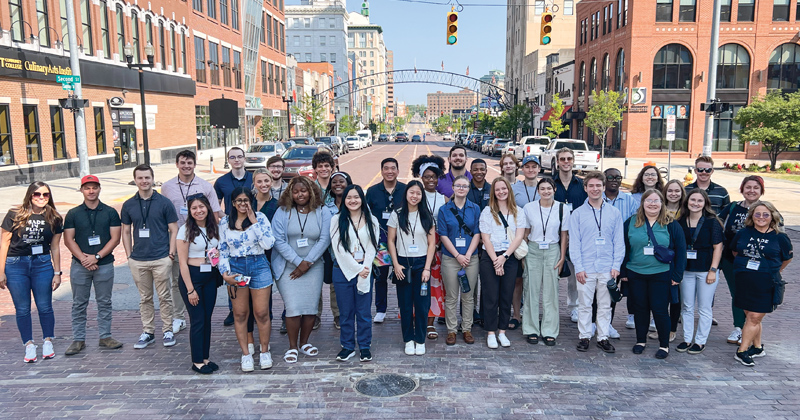 Thirty-one college students in the Flintern program and two program directors line up on Saginaw Street to get a group photo taken.