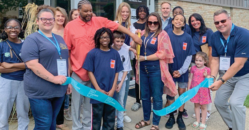 Staff and chamber members line up in back of a large blue ribbon for a ribbon cutting outside the 2nd Street Learning building.