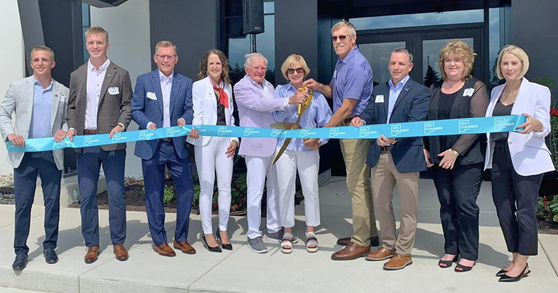 Staff and chamber members line up in back of a large blue ribbon outside the Fessler & Bowman offices for a ribbon cutting 