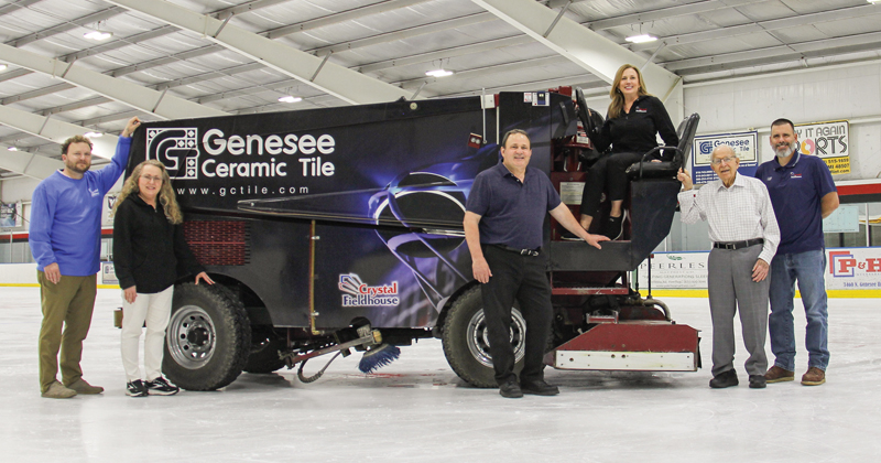 The owners and their family members stand next to a Zamboni machine on the ice at Crystal Fieldhouse