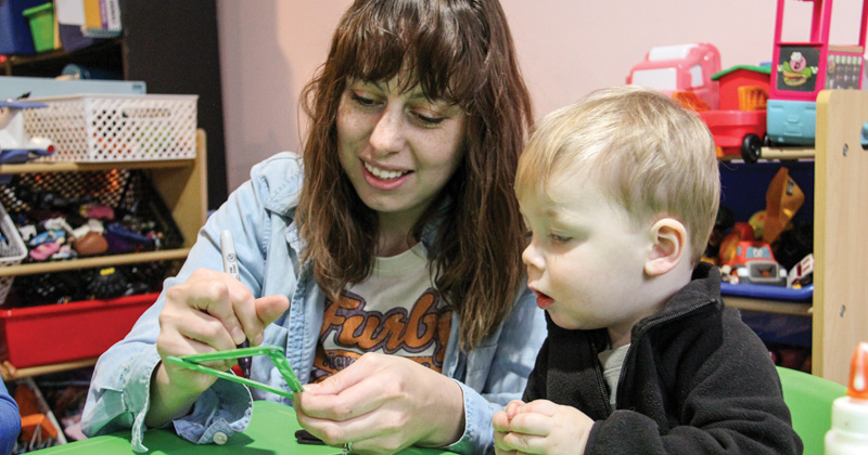 A child care worker helps a young boy making a craft project.