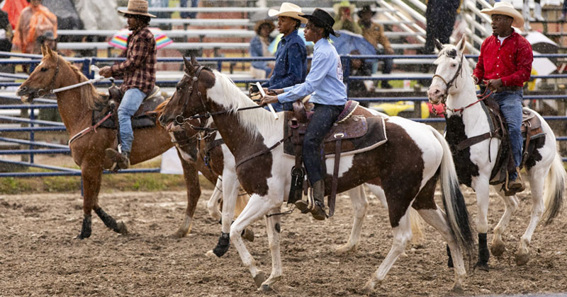 Four young cowboys ride their horses into the arena at the fairgrounds at the start of a rodeo. 