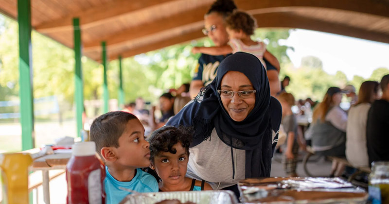 A mother helps her young son and daughter fill their plates at a picnic.