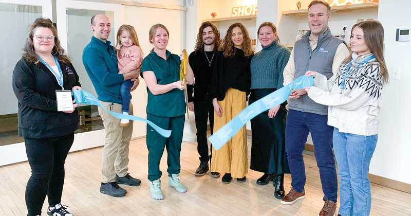 Employees at a ribboncutting event line up inside a massage studio to cut a ribbon with extra large scissors