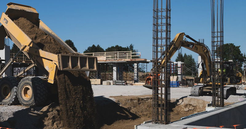 A dump truck empties a load of soil to fill in a foundation being poured.