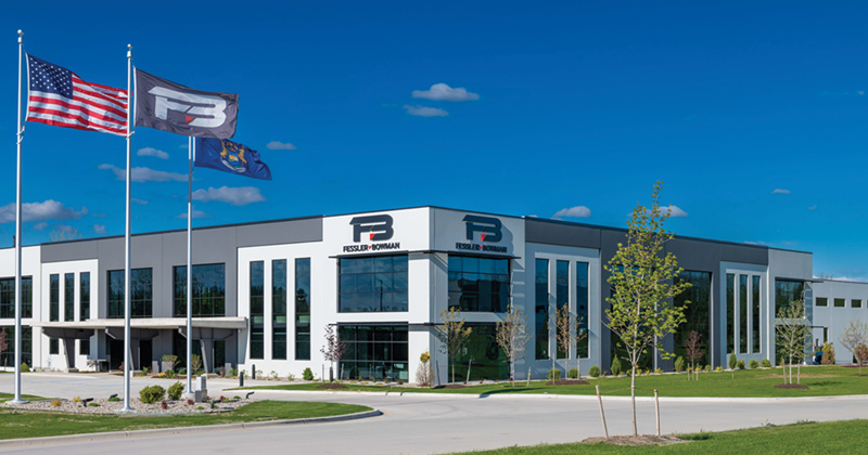 Outside view of the new Fessler & Bowman headquarters. Three large flag poles flying the U.S., Fessler & Bowman, and State of Michigan flags stand in front of the front doors.