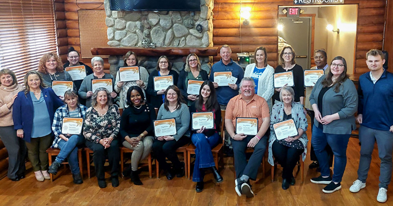 Two rows of people hold their five year certificates as certified tourism ambassadors.