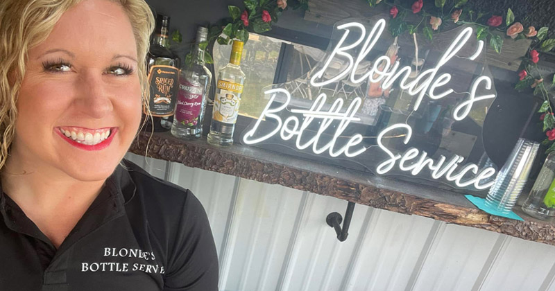 The owner of Bonde's Bottle Service smiles as she stands in front of her mobile bar which is stocked with bottles of alcohol.